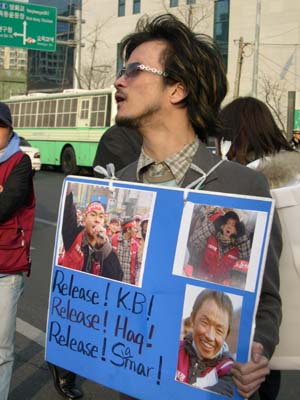 한 시위 참가자가 표적 연행된 샤멀 타파(여수)와 케비, 헉(화성) 동지들의 사진이 든 광고판을 들고 있다. 